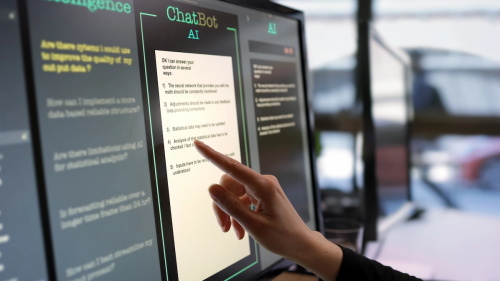 Hand touching touchscreen monitor displaying AI chatbot interface with text responses