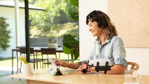 Woman wearing non-invasive brain neurotherapy headset and hand rehabilitation robotic brace using tablet at home